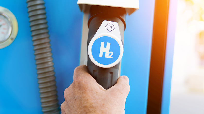 Un hombre sostiene un surtidor de combustible con el logotipo del hidrógeno en una estación de servicio. Motor de combustión h2 para un transporte ecológico sin emisiones.